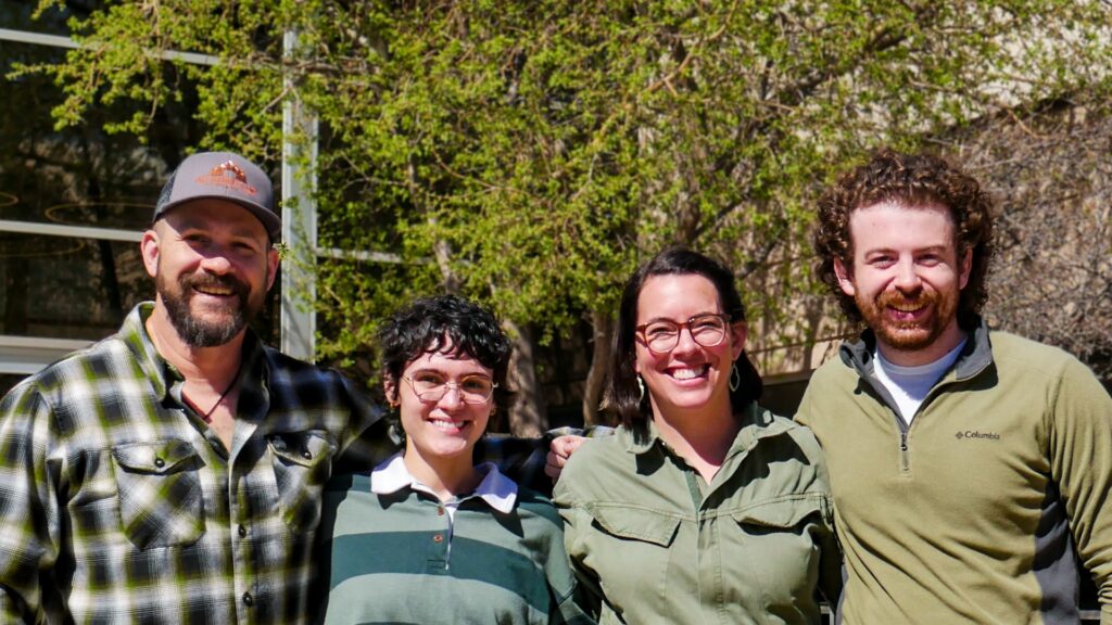 four people standing outside the JCC, smiling. Two men on the outside and two women. Most wear green to represent their membership on the Green Team